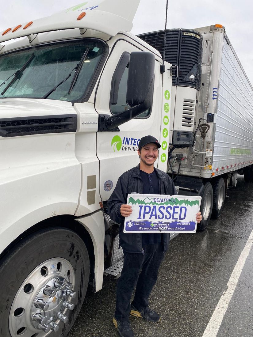 Integrity Driving School Class 1 MELT graduate holding an I Passed sign beside a Freightliner Cascadia tractor and reefer trailer